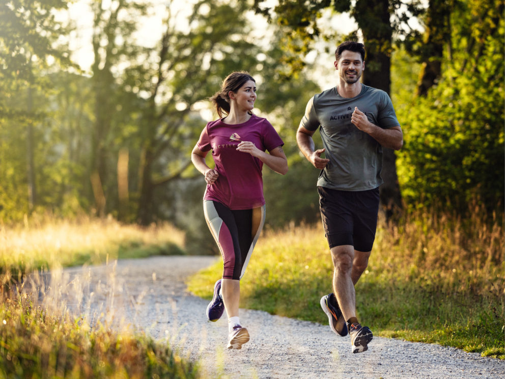 Zwei Personen joggen beim schönen Wetter einen Waldweg entlang.